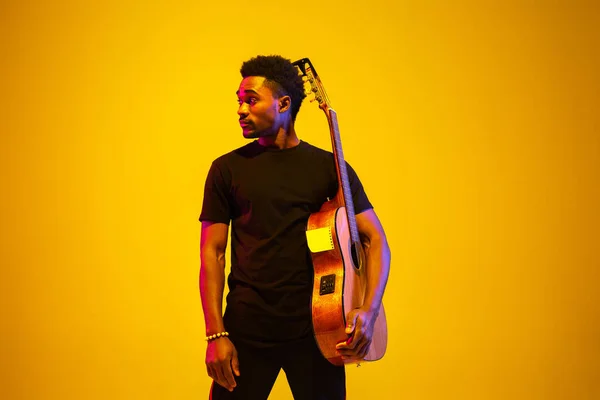 Jonge Afrikaans-Amerikaanse muzikant die zingt, gitaar speelt in neon licht — Stockfoto