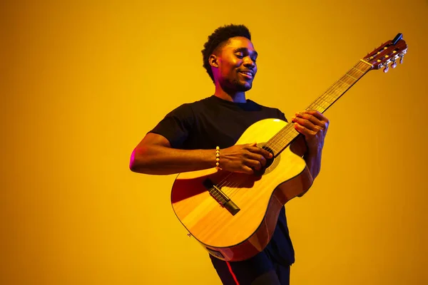 Joven músico afroamericano cantando, tocando la guitarra en luz de neón — Foto de Stock