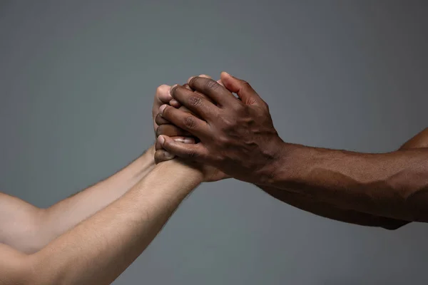 Tolerancia racial. Respetar la unidad social. Africano y caucásico manos gesto aislado en gris estudio fondo — Foto de Stock