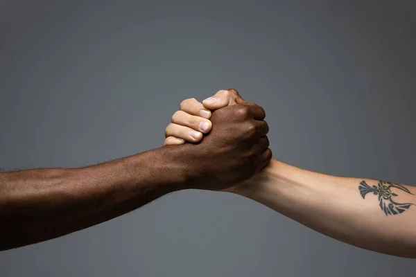 Tolerancia racial. Respetar la unidad social. Africano y caucásico manos gesto aislado en gris estudio fondo —  Fotos de Stock