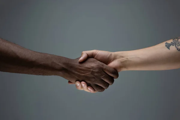 Tolerancia racial. Respetar la unidad social. Africano y caucásico manos gesto aislado en gris estudio fondo — Foto de Stock