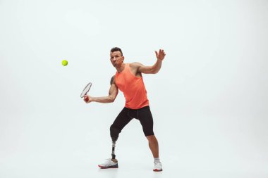 Engelli ya da sakatlığı olan bir sporcu beyaz stüdyo arka planında izole edilmiş. Profesyonel erkek tenisçi, bacak protezi eğitimi almış ve stüdyoda pratik yapıyor..