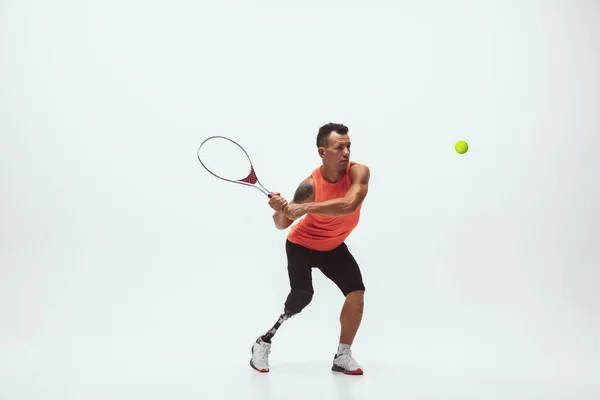 Athlete with disabilities or amputee isolated on white studio background. Professional male tennis player with leg prosthesis training and practicing in studio.
