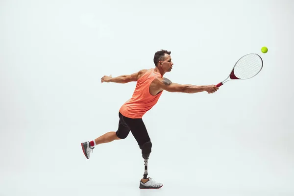 Athlete with disabilities or amputee isolated on white studio background. Professional male tennis player with leg prosthesis training and practicing in studio.