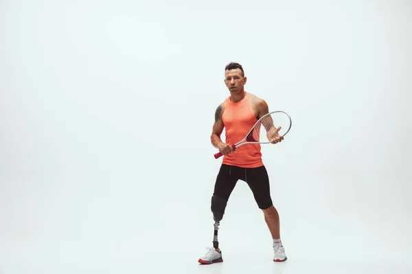 Athlete with disabilities or amputee isolated on white studio background. Professional male tennis player with leg prosthesis training and practicing in studio.