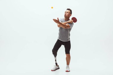 Engelli ya da sakatlığı olan bir sporcu beyaz stüdyo arka planında izole edilmiş. Profesyonel masa tenisi oyuncusu, bacak protezi eğitimi almış ve stüdyoda pratik yapıyor..