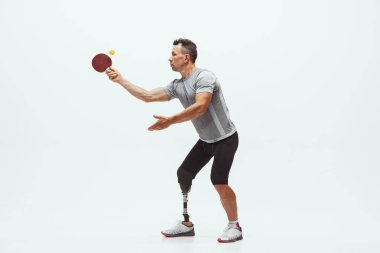 Engelli ya da sakatlığı olan bir sporcu beyaz stüdyo arka planında izole edilmiş. Profesyonel masa tenisi oyuncusu, bacak protezi eğitimi almış ve stüdyoda pratik yapıyor..