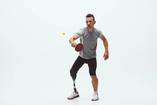 Athlete with disabilities or amputee isolated on white studio background. Professional male table tennis player with leg prosthesis training and practicing in studio.