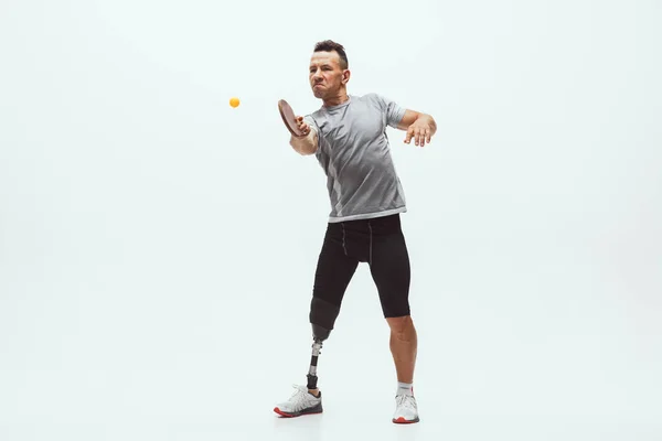Athlete with disabilities or amputee isolated on white studio background. Professional male table tennis player with leg prosthesis training and practicing in studio.