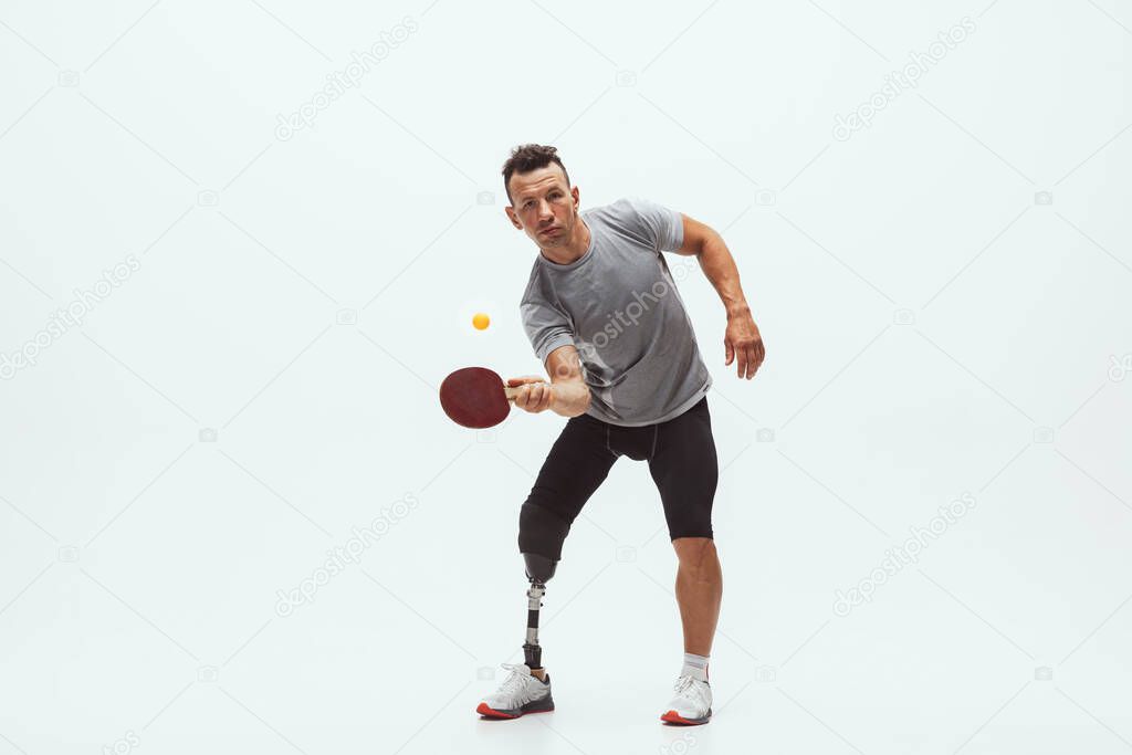 Athlete with disabilities or amputee isolated on white studio background. Professional male table tennis player with leg prosthesis training and practicing in studio.