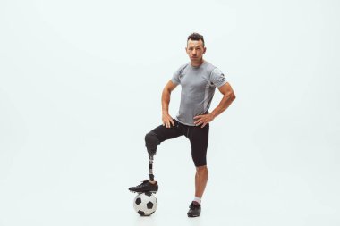 Athlete with disabilities or amputee isolated on white studio background. Professional male football player with leg prosthesis training and practicing in studio. clipart