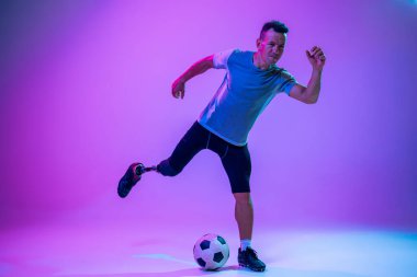 Stüdyonun arka planında engelli ya da sakatlığı olan bir sporcu izole edilmiş. Profesyonel erkek futbolcu, bacak protezi eğitimi almış ve stüdyoda pratik yapıyor..