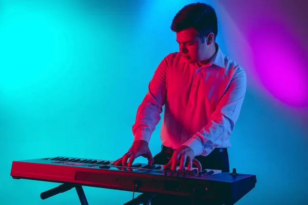 Fiatal kaukázusi zenész, billentyűs, lejtős háttérben játszik neonfényben. Koncepciója zene, hobbi, fesztivál — Stock Fotó