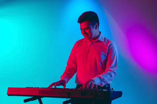 Joven músico caucásico, tecladista tocando sobre fondo degradado en luz de neón. Concepto de música, hobby, festival — Foto de Stock