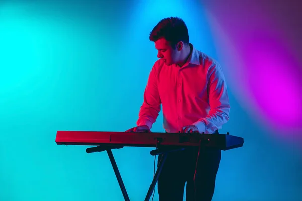 Junger kaukasischer Musiker, Keyboarder, der auf einem Gradienten-Hintergrund im Neonlicht spielt. Konzept Musik, Hobby, Festival — Stockfoto