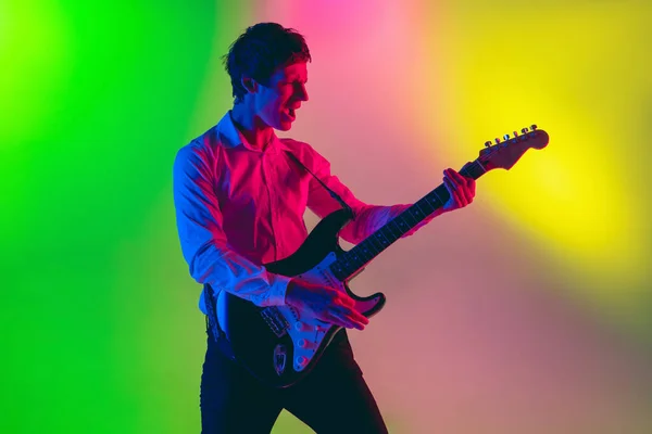 Jovem músico caucasiano, guitarrista tocando em fundo gradiente em luz de néon. Conceito de música, hobby, festival — Fotografia de Stock