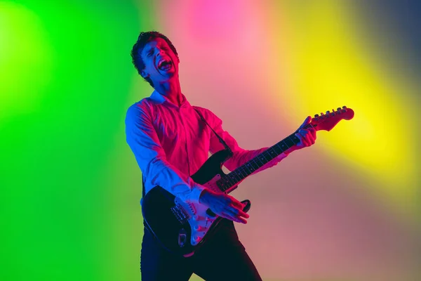 Junger kaukasischer Musiker, Gitarrist, der auf einem Gradienten-Hintergrund im Neonlicht spielt. Konzept Musik, Hobby, Festival — Stockfoto
