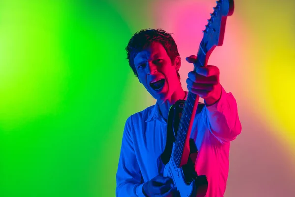 Jovem músico caucasiano, guitarrista tocando em fundo gradiente em luz de néon. Conceito de música, hobby, festival — Fotografia de Stock