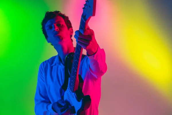 Joven músico caucásico, guitarrista tocando sobre fondo degradado en luz de neón. Concepto de música, hobby, festival — Foto de Stock