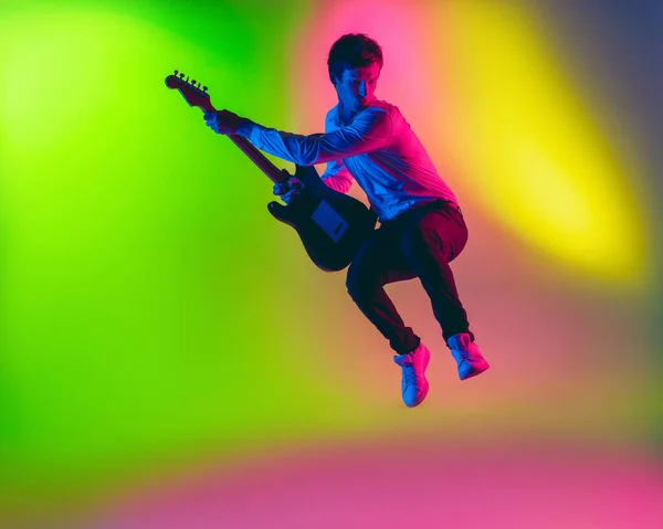 Jonge Kaukasische muzikant, gitarist op een gradiënt achtergrond in neon licht. Concept van muziek, hobby, festival — Stockfoto