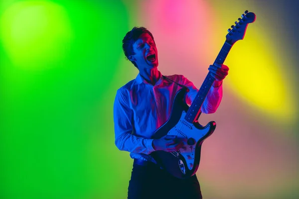 Jovem músico caucasiano, guitarrista tocando em fundo gradiente em luz de néon. Conceito de música, hobby, festival — Fotografia de Stock