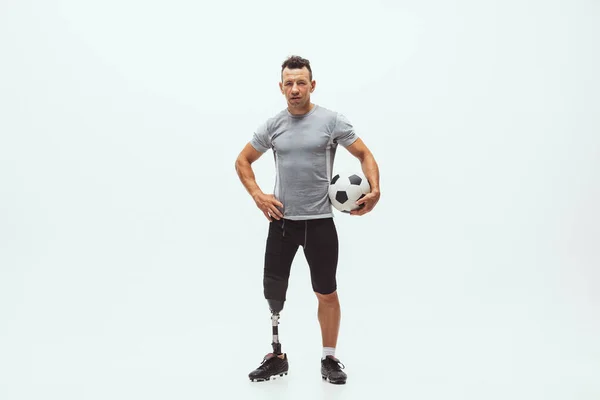 Athlete with disabilities or amputee isolated on white studio background. Professional male football player with leg prosthesis training and practicing in studio.