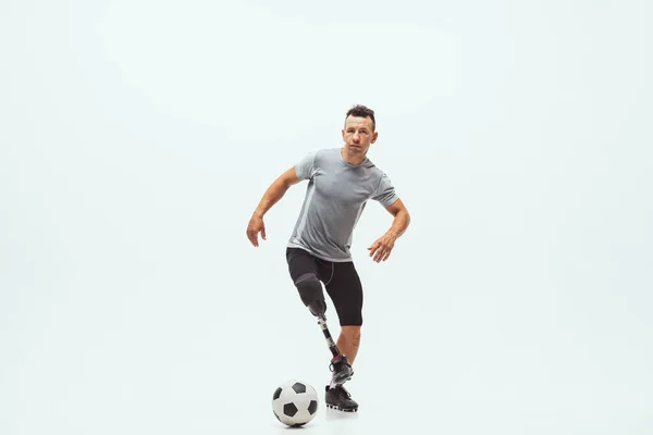 Atleta con discapacidad o amputado aislado en el fondo blanco del estudio. Jugador de fútbol masculino profesional con entrenamiento de prótesis de pierna y práctica en estudio . —  Fotos de Stock