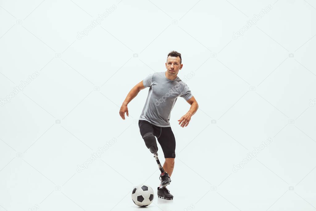 Athlete with disabilities or amputee isolated on white studio background. Professional male football player with leg prosthesis training and practicing in studio.