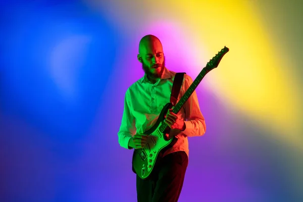 Junger kaukasischer Musiker, Gitarrist, der auf einem Gradienten-Hintergrund im Neonlicht spielt. Konzept Musik, Hobby, Festival — Stockfoto