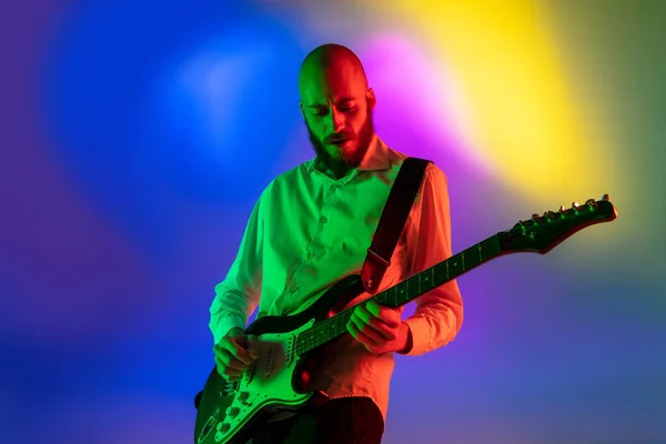 Fiatal kaukázusi zenész, gitáros, aki lejtős háttérrel játszik neonfényben. Koncepciója zene, hobbi, fesztivál — Stock Fotó