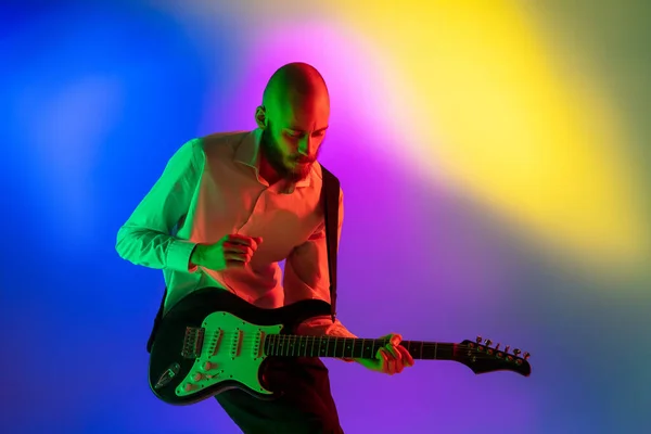 Junger kaukasischer Musiker, Gitarrist, der auf einem Gradienten-Hintergrund im Neonlicht spielt. Konzept Musik, Hobby, Festival — Stockfoto
