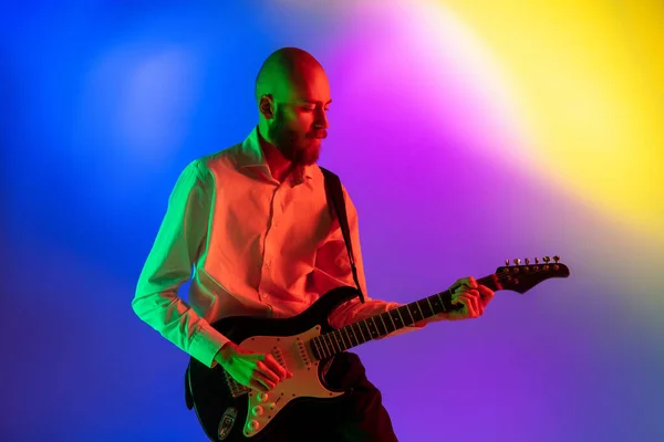 Jovem músico caucasiano, guitarrista tocando em fundo gradiente em luz de néon. Conceito de música, hobby, festival — Fotografia de Stock