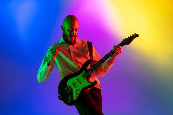 Joven músico caucásico, guitarrista tocando sobre fondo degradado en luz de neón. Concepto de música, hobby, festival — Foto de Stock