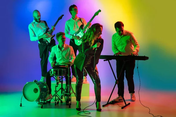 Jovens músicos caucasianos, banda tocando em fundo gradiente em luz de néon. Conceito de música, hobby, festival — Fotografia de Stock