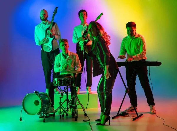 Jovens músicos caucasianos, banda tocando em fundo gradiente em luz de néon. Conceito de música, hobby, festival — Fotografia de Stock