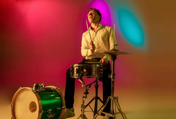 Ung kaukasisk musiker, trummis spelar på lutning bakgrund i neonljus. Begreppet musik, hobby, festival — Stockfoto