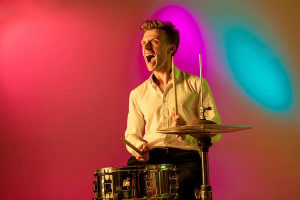 Jovem músico caucasiano, baterista tocando em fundo gradiente em luz de néon. Conceito de música, hobby, festival — Fotografia de Stock