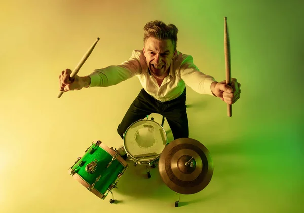 Jovem músico caucasiano, baterista tocando em fundo gradiente em luz de néon. Conceito de música, hobby, festival — Fotografia de Stock