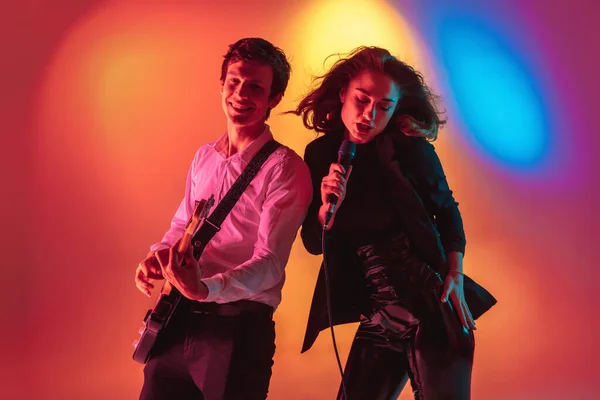 Junge kaukasische Musiker, Sängerinnen und Gitarristinnen, die auf einem Gefälluntergrund im Neonlicht auftreten. Konzept Musik, Hobby, Festival — Stockfoto
