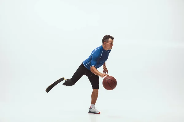 Athlete with disabilities or amputee isolated on white studio background. Professional male basketball player with leg prosthesis training and practicing in studio.