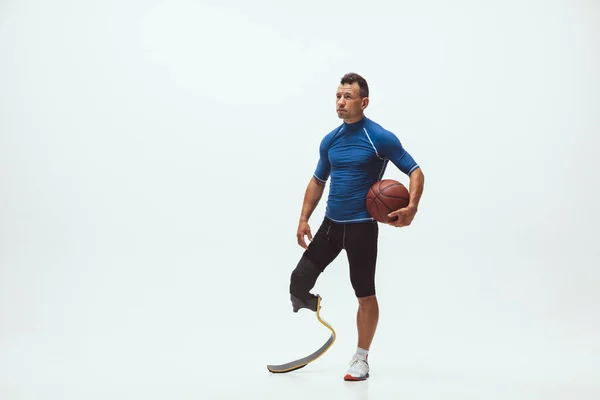 Athlete with disabilities or amputee isolated on white studio background. Professional male basketball player with leg prosthesis training and practicing in studio. — Stock Photo, Image