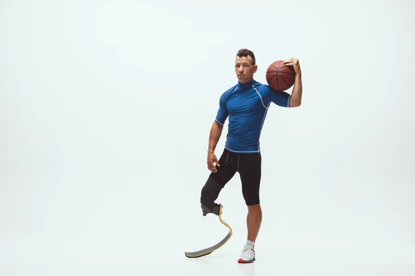 Athlete with disabilities or amputee isolated on white studio background. Professional male basketball player with leg prosthesis training and practicing in studio. — Stock Photo, Image