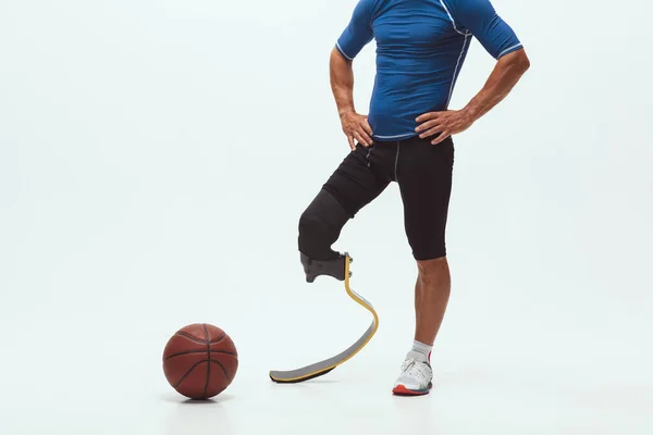 Athlete with disabilities or amputee isolated on white studio background. Professional male basketball player with leg prosthesis training and practicing in studio.