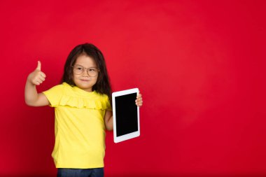 Kırmızı arka planda izole edilmiş güzel, duygusal küçük bir kız. Mutlu çocuk hareketlerinin yarım boy portresi