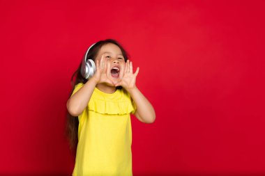 Kırmızı arka planda izole edilmiş güzel, duygusal küçük bir kız. Mutlu çocuk hareketlerinin yarım boy portresi