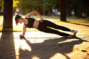 Genç bayan sporcu yaz güneşinde şehir caddesinde antrenman yapıyor. Egzersiz yapan güzel bir kadın. Spor anlayışı, sağlıklı yaşam tarzı, hareket, aktivite.