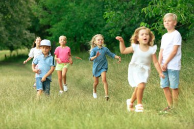 Çocuklar, çocuklar yaz güneşinde çayırda koşuyorlar.