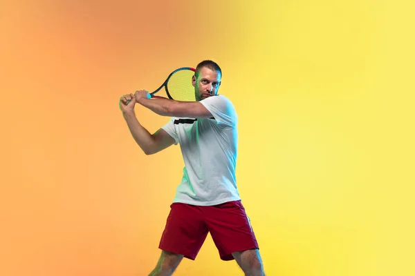 Hombre caucásico deportista profesional jugando al tenis en el fondo del estudio en luz de neón — Foto de Stock