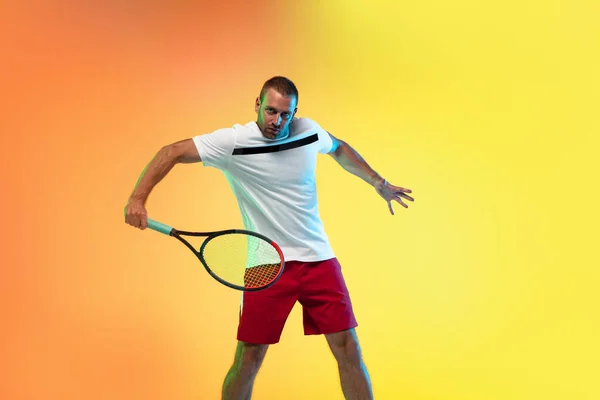 Hombre caucásico deportista profesional jugando al tenis en el fondo del estudio en luz de neón —  Fotos de Stock