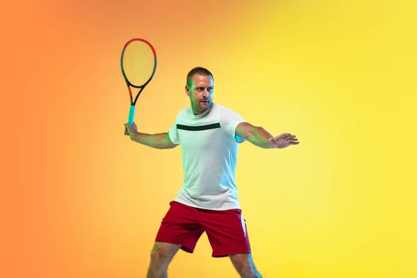 Hombre caucásico deportista profesional jugando al tenis en el fondo del estudio en luz de neón —  Fotos de Stock